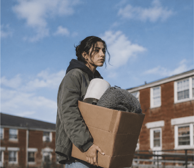 A woman carrying a box full of personal belongings outside an apartment complex
